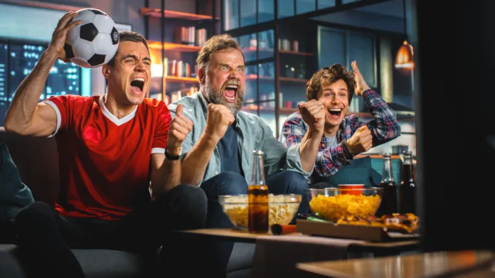 Night At Home: Three Joyful Soccer Fans on a Couch Watch Game on TV, Celebrate Victory when Sports Team Wins Championship. Friends Cheer for Favourite Football Club Play.