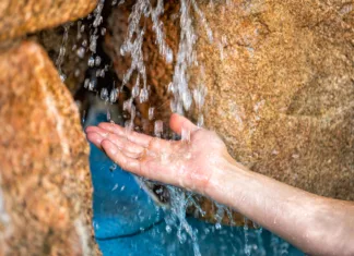 Kopanje v mineralni vodi priporočljivo za srčno-žilna obolenja Young man hands closeup with water splash drops in Japanese hot spring onsen spa by stone pool colorful blue water and waterfall in Japan