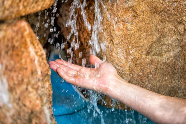 Young man hands closeup with water splash drops in Japanese hot spring onsen spa by stone pool colorful blue water and waterfall in Japan