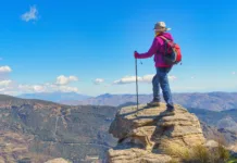 Najvišja priznanja planinske zveze za leto 2015 poklon prizadevnim prostovoljcem A woman on top of a rock, with backpack and hiking poles, looking towards the horizon and enjoying the impressive landscape of mountains and valleys at her feet, surrounded by nature and fresh air