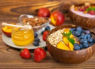 Nov sladki hit: kosmiči izMUESLI Granola bowl with yogurt and fresh almonds, blueberries, raspberries,peach and strawberries on a kitchen table.Acai and spirulina bowl.Healthy breakfast concept.copy space.Place for text.