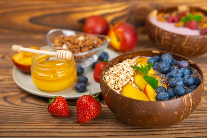 Granola bowl with yogurt and fresh almonds, blueberries, raspberries,peach and strawberries on a  kitchen table.Acai and spirulina bowl.Healthy breakfast concept.copy space.Place for text.