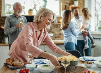 Sobivanje s ‘tamladimi’: prednosti, slabosti in nasveti za harmoničen skupen dom Happy mature woman having lunch with her family and serving food on dining table.