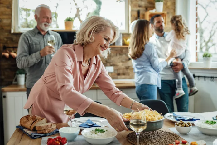 Happy mature woman having lunch with her family and serving food on dining table.