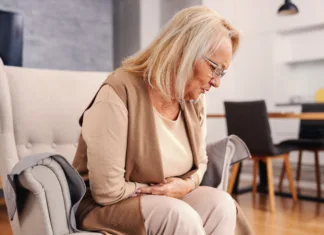 Zaprtje: kako do olajšanja v 15 minutah? Sick senior woman sitting at home in her chair and holding her stomach. She is in pain.
