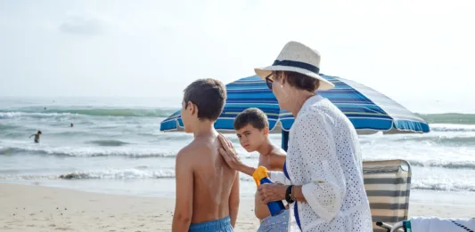 A grandmother putting sunscreen on her grandchildren at the beach. Summer skin care concept