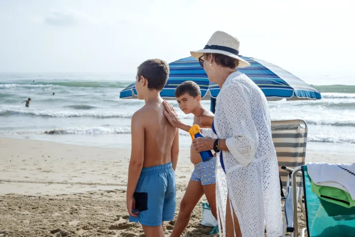 A grandmother putting sunscreen on her grandchildren at the beach. Summer skin care concept