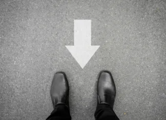 Hoja ‘v rikverc’: Poznate vse koristi? Businessman in black shoes standing on asphalt concrete road and direction sign backward. Wrong way and have to go back.