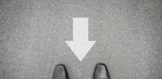 Businessman in black shoes standing on asphalt concrete road and direction sign backward. Wrong way and have to go back.
