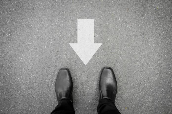 Businessman in black shoes standing on asphalt concrete road and direction sign backward. Wrong way and have to go back.