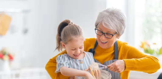 Happy loving family are preparing bakery together. Granny and child are cooking cookies and having fun in the kitchen.