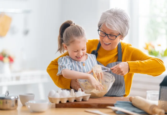 Happy loving family are preparing bakery together. Granny and child are cooking cookies and having fun in the kitchen.