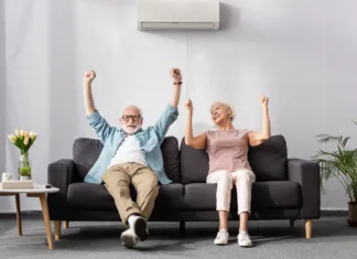 Na takšno temperaturo bi morali nastaviti klimatsko napravo Positive senior couple showing yeah gesture while sitting on couch in living room