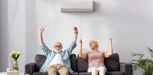 Positive senior couple showing yeah gesture while sitting on couch in living room