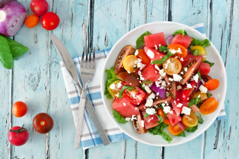 Watermelon and mixed tomato salad with feta cheese, overhead scene on rustic blue wood