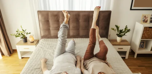 A senior couple is lying on a bed at home and doing morning gymnastic.
