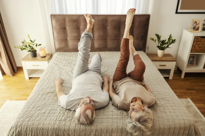 A senior couple is lying on a bed at home and doing morning gymnastic.