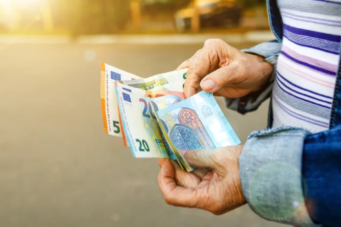 Euro banknotes in hands of elderly woman. Pension payments in Europe, retirement savings or benefits concept, female pensioner with paper currency of EU. Selective focus, close-up