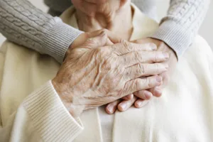 Mature female in elderly care facility gets help from hospital personnel nurse. Senior woman, aged wrinkled skin & hands of her care giver. Grand mother everyday life. Background, copy space, close up