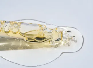 Kaj je kolagen, kje ga najdemo in zakaj ga je smiselno uživati? Bottle pipette dropper close up and Liquid yellow-orange retinol or vitamin c gel or serum on a blue background