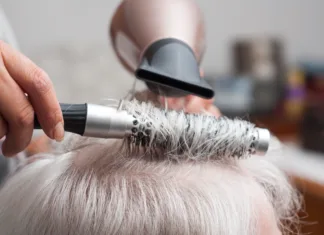 Nega las v starejšem življenjskem obdobju Closeup of hands of hairdresser on old woman with gray hairs - hairdresser at home concept
