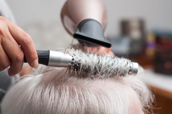 Closeup of hands of hairdresser on old woman with gray hairs - hairdresser at home concept