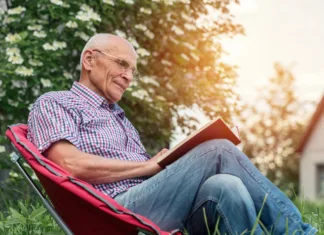 Nacionalni mesec skupnega branja: Poznate vse koristi branja? Retired man seated on armchair wearing glasses reading book in garden outdoor of cottage house.