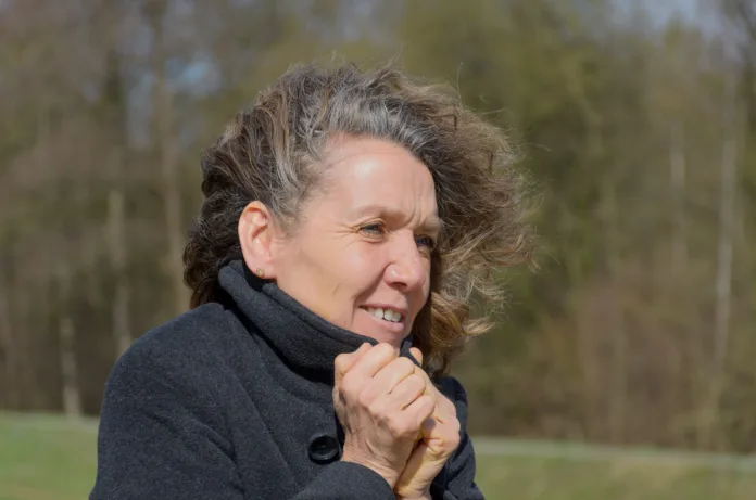 Woman snuggling into her jacket on a windy cold day with her long hair blowing to the side in the breeze in a rural landscape