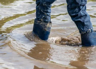Lastniki v poplavah poškodovanih stanovanj bodo prejeli pozive za posredovanje dokazil Young boy with short blue trowsers wading with wet socks and wet boots through high tide after a floodwater has broken the dike and overflown the lands behind
