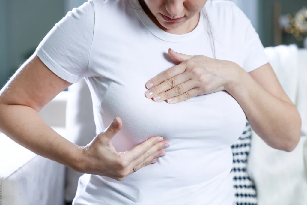 Young clothed woman doing preliminary breast self-check at home