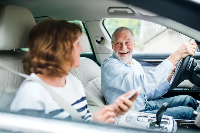 A happy senior couple with smartphone sitting in car, going on trip.