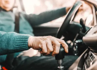Bi starejši morali voziti avto z avtomatskim menjalnikom? Close up of senior man holding one hand on gearshift and other on steering wheel while sitting in his car. Selective focus on hand.