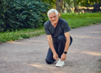 Najpogostejše napake pri izbiri obutve za starejše – Ali jih delate tudi vi? Elderly man in sportive wear ties shoelaces ready for morning jogging or sportive walk stroll in summer park smile look at camera. Healthy active lifestyle of retiree, work out