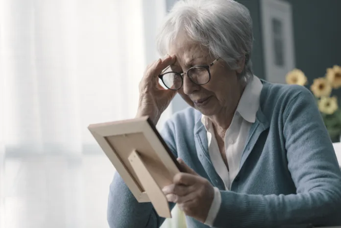 Sad woman at home grieving the loss of her husband, she is holding a picture and crying