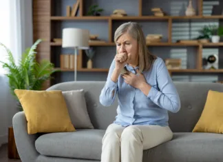 Okrepite imunski sistem z močjo narave Senior stylish woman feeling sick and covering mouth with clenched fist for stopping cough while sitting on sofa with cushions. Unhealthy female feeling pain in chest and suffering from flu symptoms.