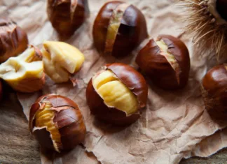 Jesenska poslastica: Zakaj je koristno uživati kostanj? Traditional Christmas dish - Ripe Sweet Roasted Chestnuts, cracked shells after put to the fire, natural paper and old wooden rustic background.