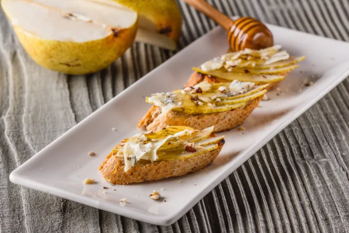 Appetizer bruschetta with pear, honey, walnut and blue cheese on white plate.