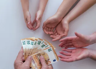 Zakaj je pomembno, da vnuke naučimo finančne pismenosti? Old grandfather or grandmother hands giving 50 euros banknotes to another pairs of hands of his her wife man and grandchildren kids