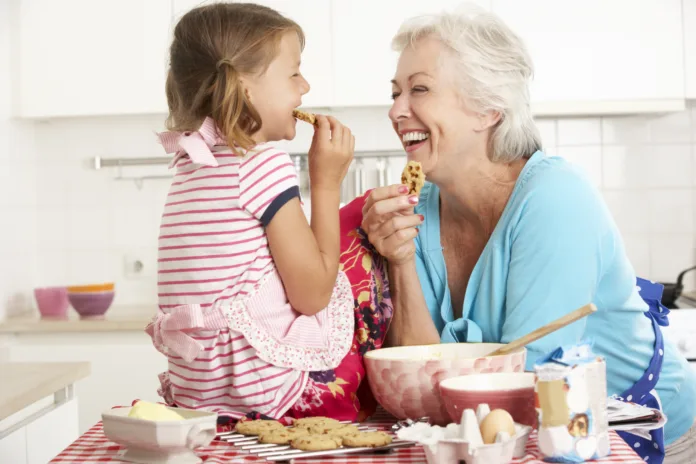 Grandmother And Granddaughter Baking In Kitchen Smiling And Laughing At Each Other.