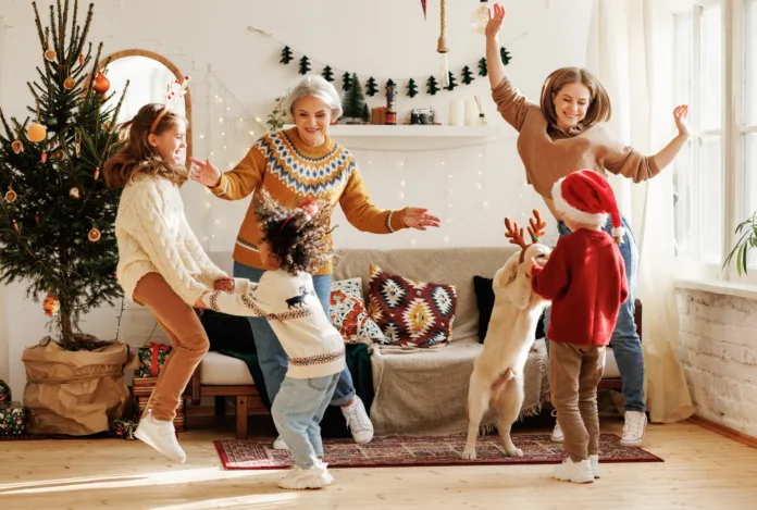 Happy positive multiracial family with three kids and golden retriever have fun on Christmas day at home. Mother, grandmother and multiethnic children dance to New Year music during winter holidays