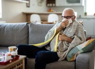 Cepljenje proti gripi: za koga je smiselno? Senior man at home suffering with cold or flu virus. Shot of a senior man blowing his nose with a tissue at home.