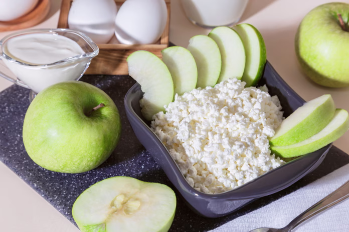 Healthy balanced nutrition, dairy products. Fresh homemade cottage cheese with fruits, eggs, cream and green sliced apple in a bowl, diet food for breakfast source of protein vitamins calcium minerals