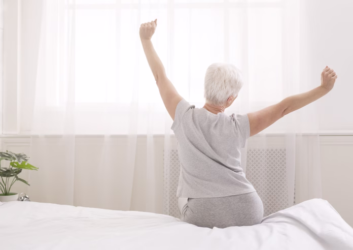 senior-woman-sitting-on-her-bed-in-morning-stretching-with-arms-raised-back-view-free-space-stockpack-istock Senior woman sitting on her bed in morning, stretching with arms raised, back view, free space