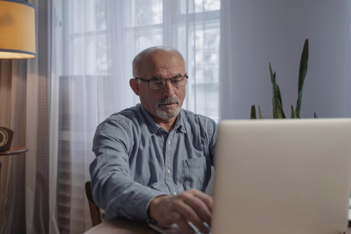 An elderly man wearing eyeglasses while looking at his laptop