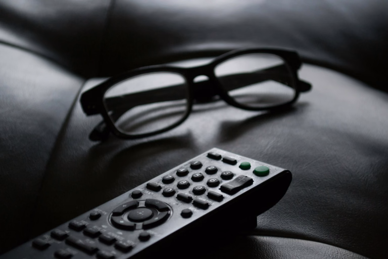 Grayscale photo of remote control near eyeglasses