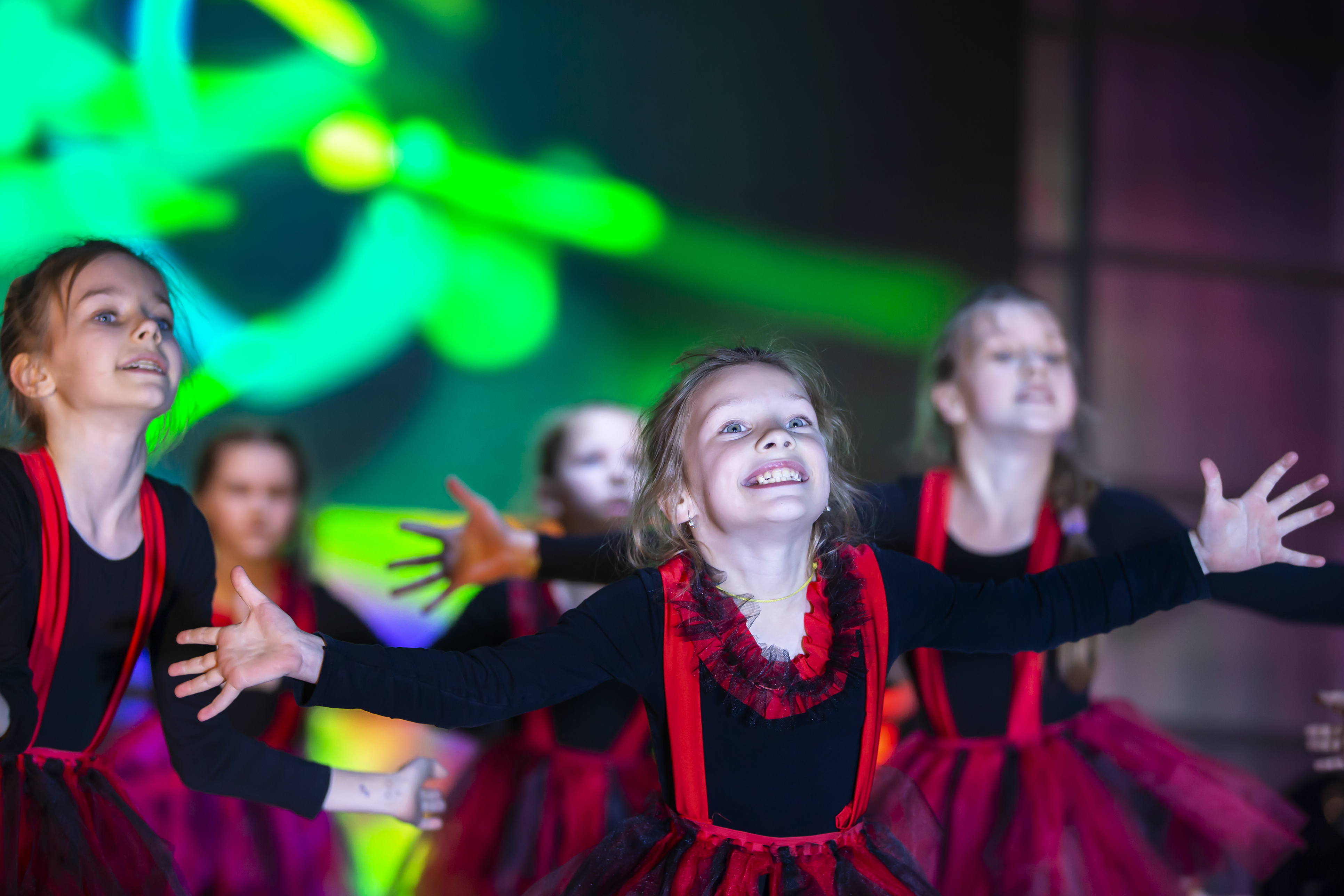 »Babica, dedek, pridita me pogledat!« Zakaj je vaša prisotnost vnukom tako pomembna Little girls are performing a dance number. Dance for Helovinna in red suits. Girl dancing. Emotional performance of a children's dance group.