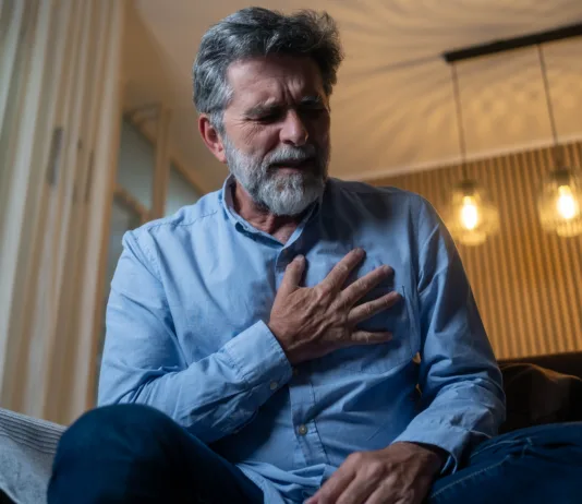 Srčni infarkt: znaki, ki jih ne smete spregledati, in kako ukrepati Mature man having a chest pain while sitting in living room at home.