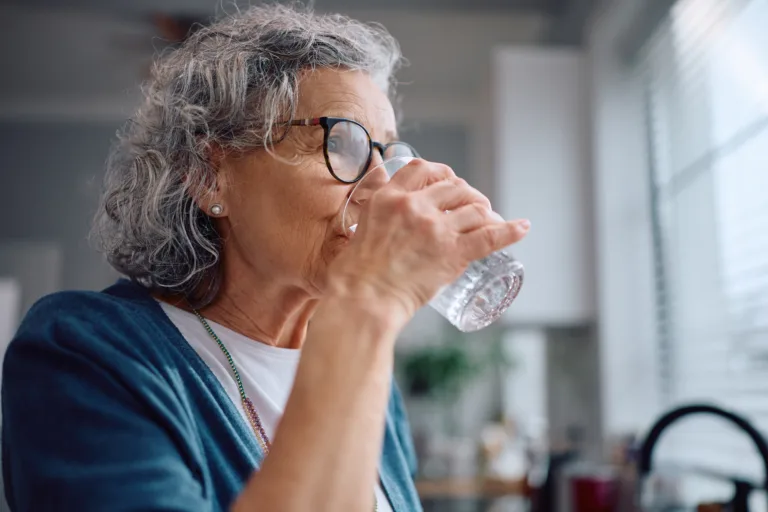 Mature woman drinking water from a glass at home.