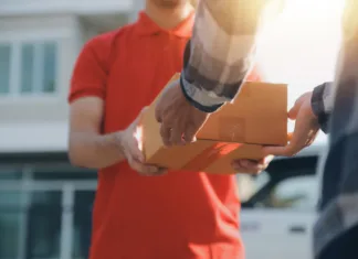 Od julija vas bodo pošiljke s Kitajske lahko pošteno udarile po žepu: Na vsak izdelek 3 evre carine Asian delivery express courier young man use giving boxes to woman customer he wearing protective face mask at front home