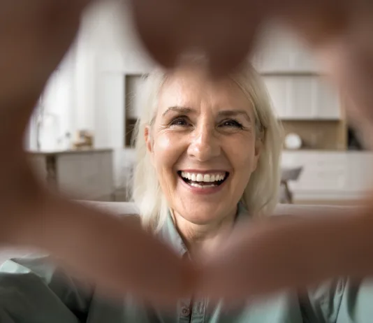 Huda vročina: pogostejši klici in obiski starejših lahko preprečijo resne težave Close up face happy older woman look at camera forming heart shape with her hands, expressing love and connection through video call, highlighting warmth and affection, share tenderness and gratitude